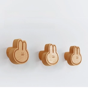 Close-up of three wooden rabbit-shaped wall hooks with natural grain on a white wall