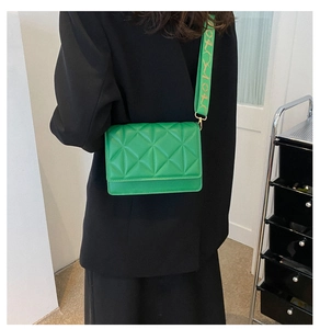 Detail of green quilted crossbody bag with a patterned wide shoulder strap on a model