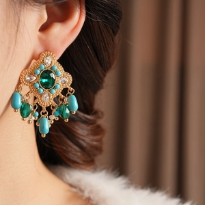 Détail de boucles d'oreilles vintage avec émeraudes et perles pendantes sur un mannequin