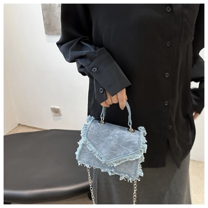 Detail of light blue denim handbag with fringe edges and silver chain strap on model