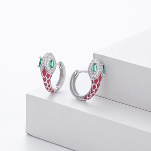 Detail of silver snake earrings with green gem eyes and red scales on white pedestal