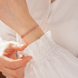 Detail of delicate pink strawberry quartz beaded bracelet on model wrist with soft lighting