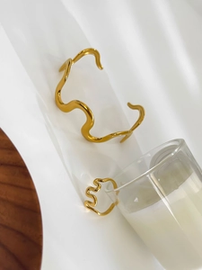 Polished gold wave-shaped bangle and ring set displayed on a white artistic base