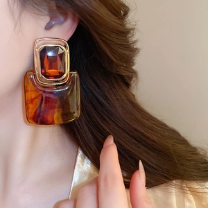 Detail of amber resin and gold square earrings worn by a model in a retro style