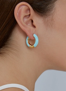 Close-up of a model wearing light blue enamel hoop earrings with gold trim detail