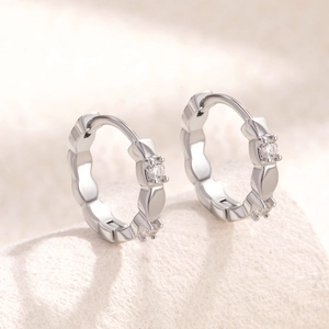 Elegant silver hoop earrings with clear cubic zirconia on a soft beige fabric surface