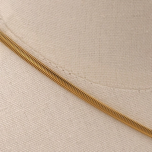 Close-up of golden stainless steel herringbone chain necklace on beige fabric