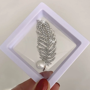 Detailed macro of a silver feather brooch with sparkling rhinestones and a white pearl