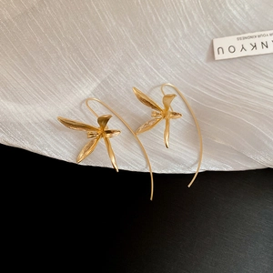 Close-up of golden iris flower earrings with curved hooks on white textured fabric