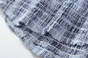 Close-up of blue plaid fabric showing smocking detail and elastic stitching on the garment