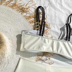 Detail of pearl white bikini top with brown straps and golden sphere metal accents