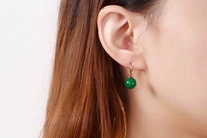 Détail de boucles d'oreilles en or rose avec perle verte portées par un mannequin