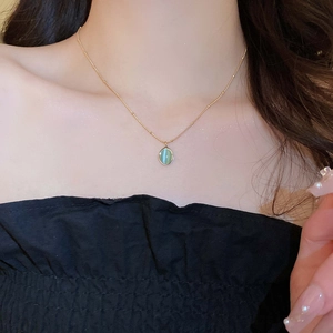 Close-up of a gold chain necklace with oval green cat-eye stone pendant on model