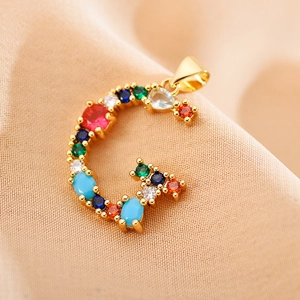 Macro view of gold letter G pendant with inlaid colorful gemstones on beige fabric