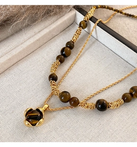 Dettaglio della collana di perle occhio di tigre con pendente bocciolo dorato