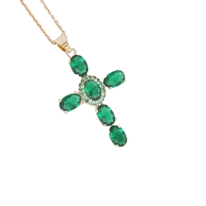 Collana dorata con pendente a croce in zircone verde smeraldo su sfondo bianco