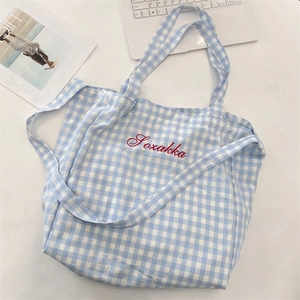 Macro detail of a blue gingham tote bag featuring red embroidery and versatile straps
