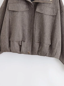 Detail of brown herringbone flight jacket showing woven texture, zipper, and metal snaps