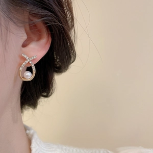Detailed close-up of an elegant pearl and zircon earring worn by a model on a beige background