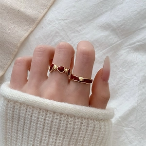 Detail of red enamel flower ring set on gold band worn on hand with cozy textile background