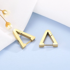 Close-up of golden geometric triangle hoop earrings on light blue textured fabric