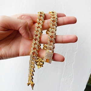 Close-up of gold Cuban link chain with paved rhinestones held in hand over white background