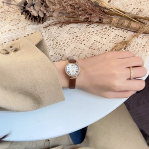 Elegant women's watch with white dial, gold crystal bezel, and slim brown leather strap