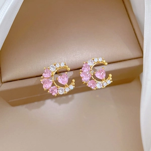 Detail of G-shaped gold stud earrings with pink heart gemstones on a beige jewelry box