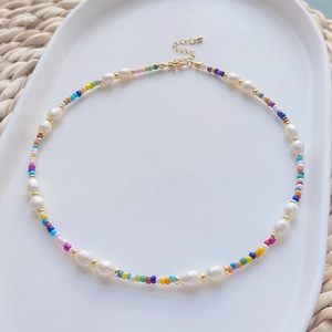 Handmade pearl and colorful bead necklace on a white ceramic tray with a boho aesthetic
