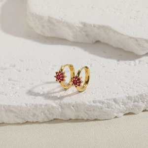 Detail view of gold hoop earrings with red floral zircon charms on white textured stone