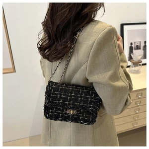 Detail of a black tweed crossbody bag with gold chain strap and metallic clasp