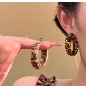 Close-up of leopard print hoop earrings on a model with warm brown background