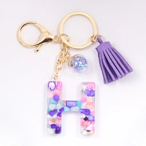 Close-up of letter H resin keychain with colorful stones and purple tassel detail