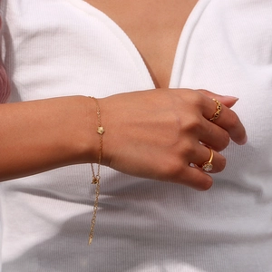 Detailed view of 18K gold plated thin bracelet with tiny floral pendant and rings