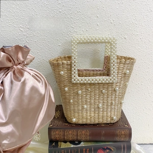 Detail view of handmade woven straw bucket bag decorated with pearls and pink satin lining