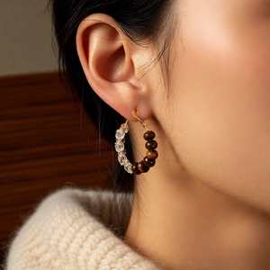 Detailed close-up of golden round hoop earrings with tiger eye stone and crystal beads