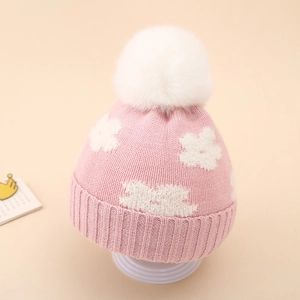 Detailed knit texture of pink baby winter hat featuring a white floral pattern and faux fur pom