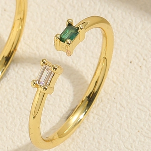 Detailed close-up of a gold open ring with emerald green and white rectangle zircons