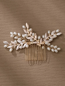 Detalle de peineta para novia con hilo dorado, hojas beige y perlas sobre fondo marrón