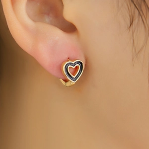 Gros plan détaillé d'une boucle d'oreille cœur dorée et émail noir portée par un modèle