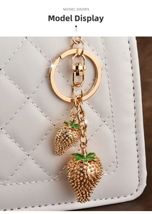 Close-up of golden strawberry charms with green enamel leaves on a white quilted bag
