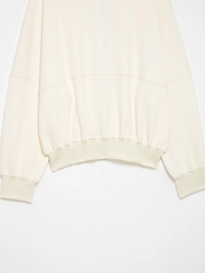 Gros plan d'un sweat-shirt crème montrant les poignets côtelés et les coutures en coton