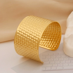 Macro view of wide gold stainless steel cuff bracelet with woven texture on soft fabric