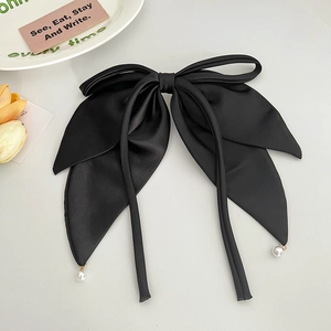 Detailed macro view of black satin bow hair clip with white pearl charms on long ribbons