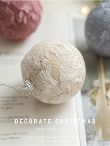 Close-up of 8cm off-white lace fabric Christmas ball with silver cap on book pages