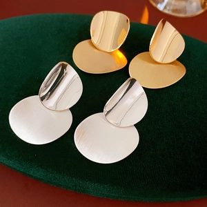 Detail of gold and silver brushed oval drop earrings on green velvet padding