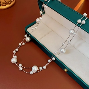 Detail of layered gold-plated necklace with irregular pearls on a green jewelry box