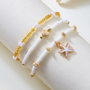 Close-up of bohemian layered bracelets with gold starfish and seashell charms on beads