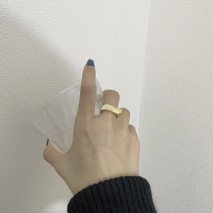 Close-up of a minimalist golden wavy ring worn on a finger with a textured background