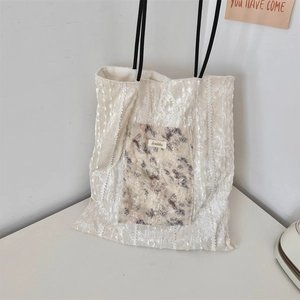 Close-up of cream canvas tote bag with floral patch, lace trim, and velvet texture